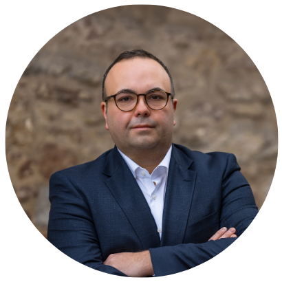 Arbeitssicherheitsansprechpartner. Porträt von Lukas Palmer, Inhaber von Palmer Arbeitssicherheit. Er schaut in die Kamera, trägt einen blauen Anzug, ein weißes Hemd und eine Brille.